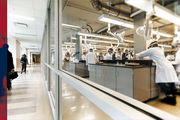 Students in white lab coats and goggles work in a lab. 