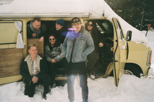 Members of The Wilderness pose in front of a van covered in snow