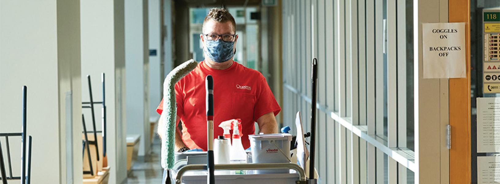 Facility services worker pushes a cart through Chernoff Hall while wearing a medical mask.