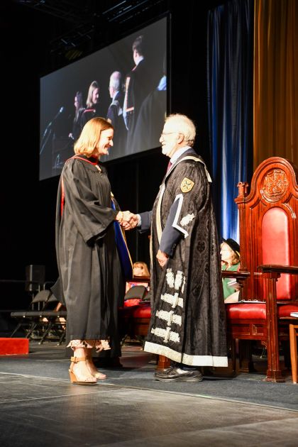 Student walking across the stage at Queen's convocation shaking hands with the Principal