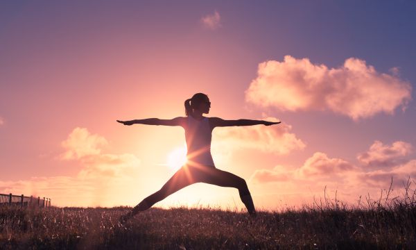 Woman doing yoga in a field with a sunset in the background