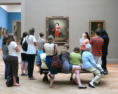 Aimee speaking to a group of people in front of various artworks.