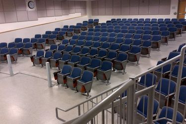 rows of fixed blue chairs in an auditorium with a grey walls