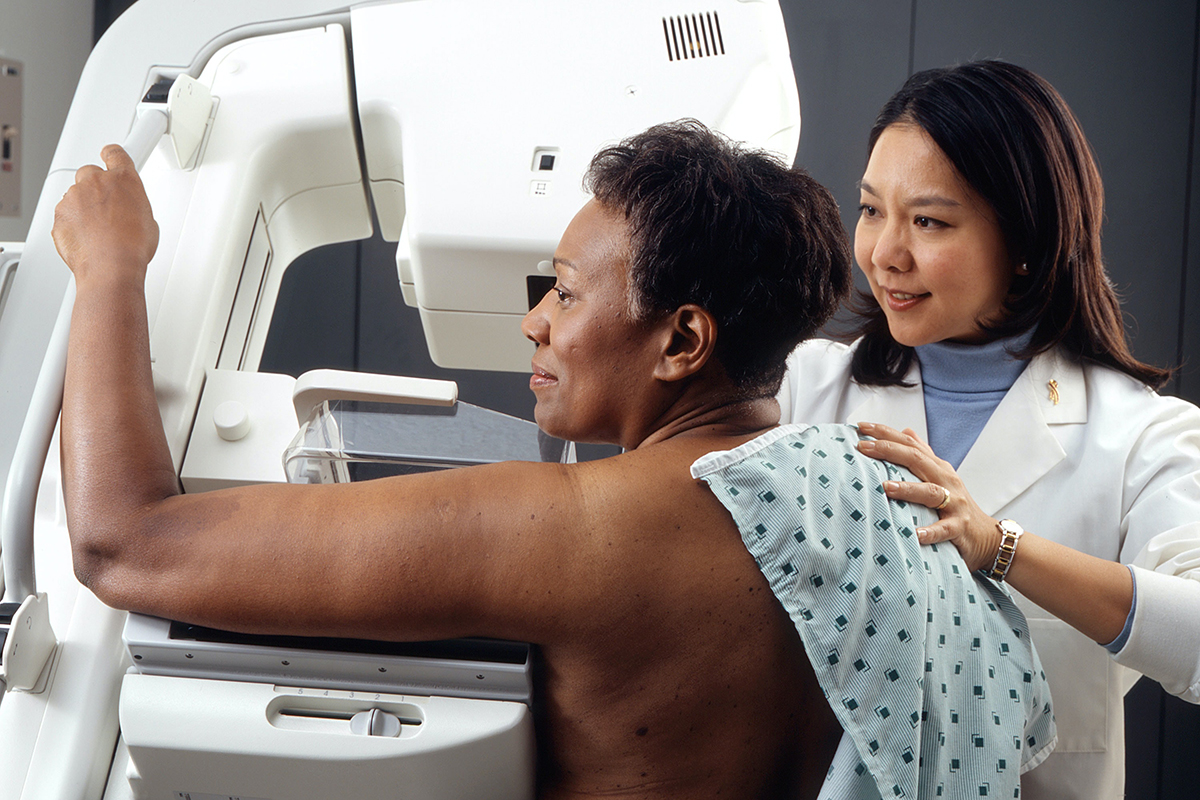 A woman gets a breast exam while a doctor helps.