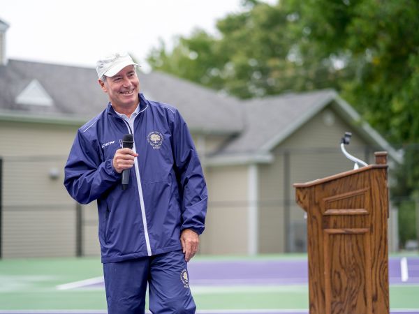 Image of Peter Smith holding a microphone on a tennis court smiling