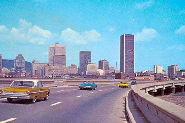 A grainy coloured photograph of 1970s cars driving down a newly built highway