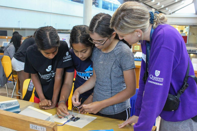 [A group of students interacting with robotics at Queen’s Connections summer program.]