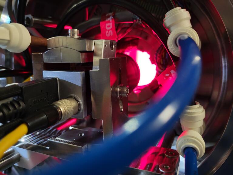 A DSLR camera with cabling and mounting hardware and a red light from the LED ring that illuminates its field of view