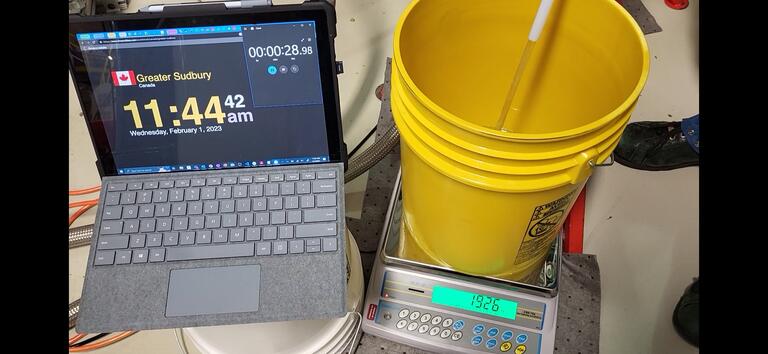 A tablet with a wall clock and a stopwatch, a scale, a pail, and chiller fluid flowing into the pail