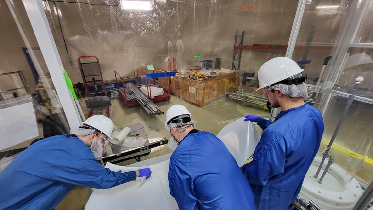 Three people work to apply retroreflector material