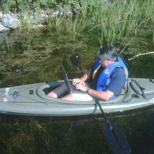 Dr. P. Stroman "working" on a laptop, while in a kayak on a lake.