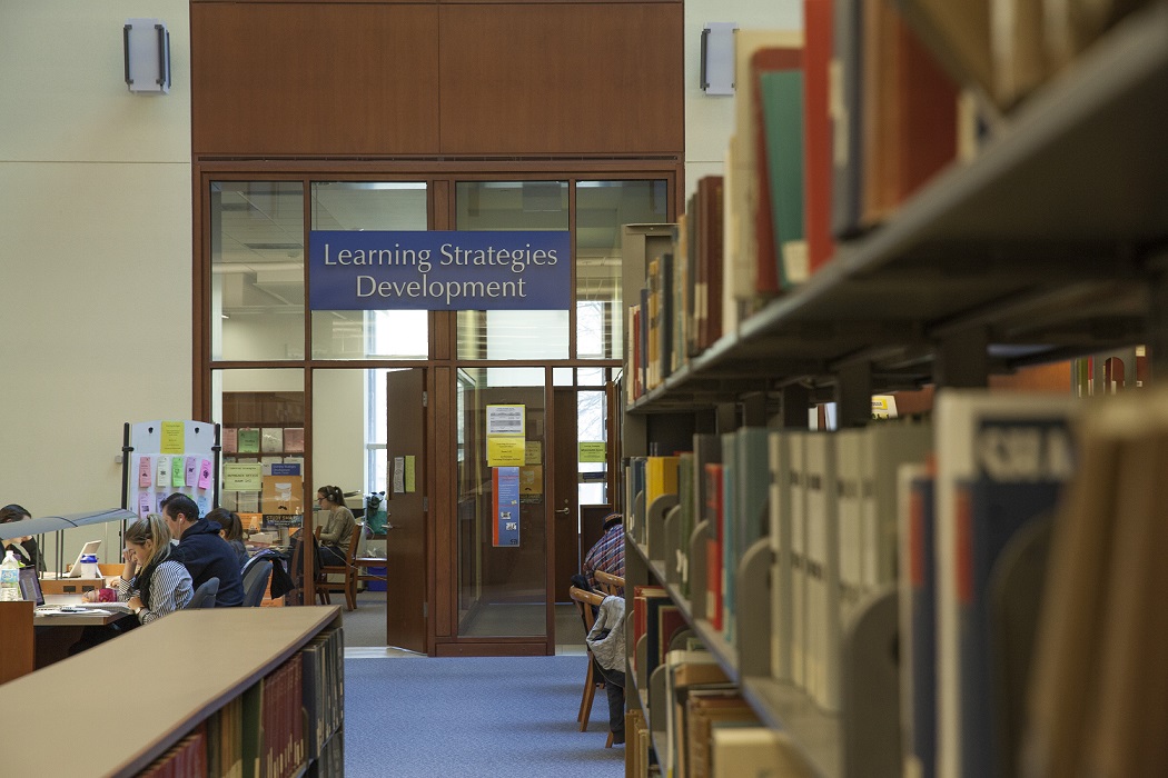 A picture from the library with books on the shelves, students studying on the left-hand side and a sign reading "Learning Strategies Development" in the far back.