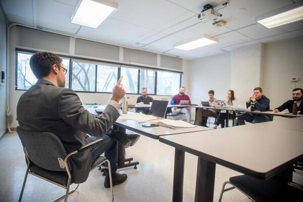A photo of the Politics Graduate and Undergraduate class in session, with the professor sitting in front of a seminar desk lecturing a group of students.