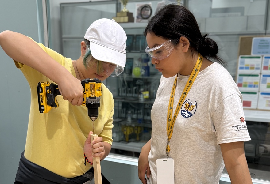 One academy participant drills a screw into a piece of wood while another watches. 