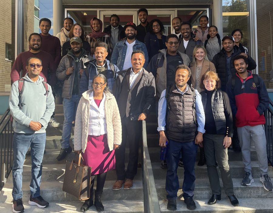 A diverse group of fellows and colleagues from Queen’s and the University of Gondar stands on steps outside a building in November 2022.