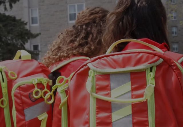 Two QFA volunteers with their bright orange backpacks on, backs to camera, facing Vic Hall