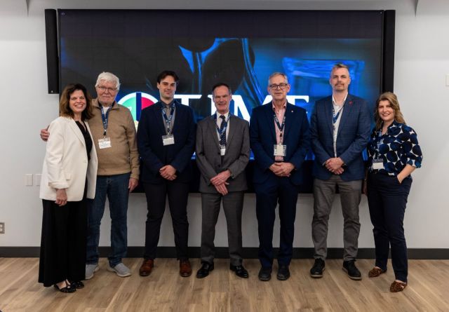 A diverse group of individuals stands before a large screen, highlighting the new W.J. Henderson TIME Collaboratory initiative at Queen’s.