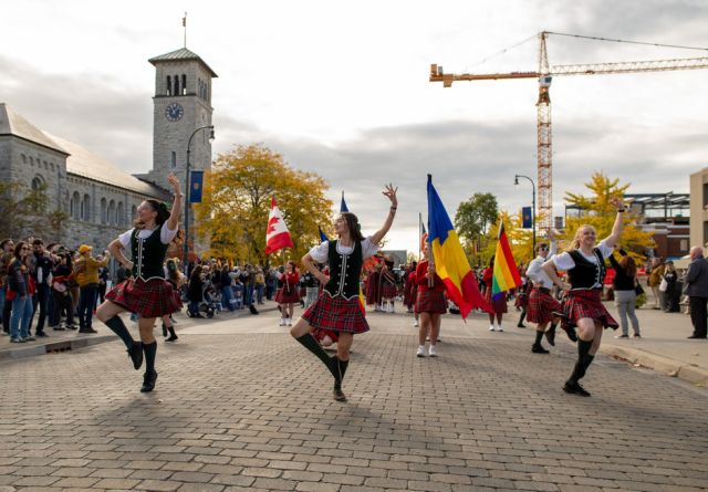 A lively street scene featuring people in kilts dancing joyfully, highlighting a festive atmosphere.