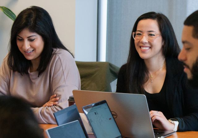 Students smiling with laptops around them.