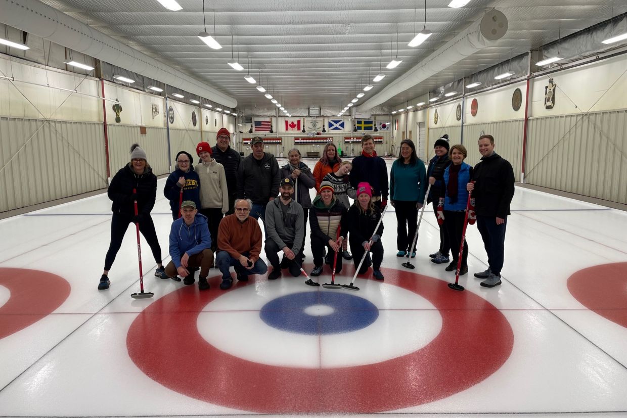 A group of alumni posing on an indoor curling rink.