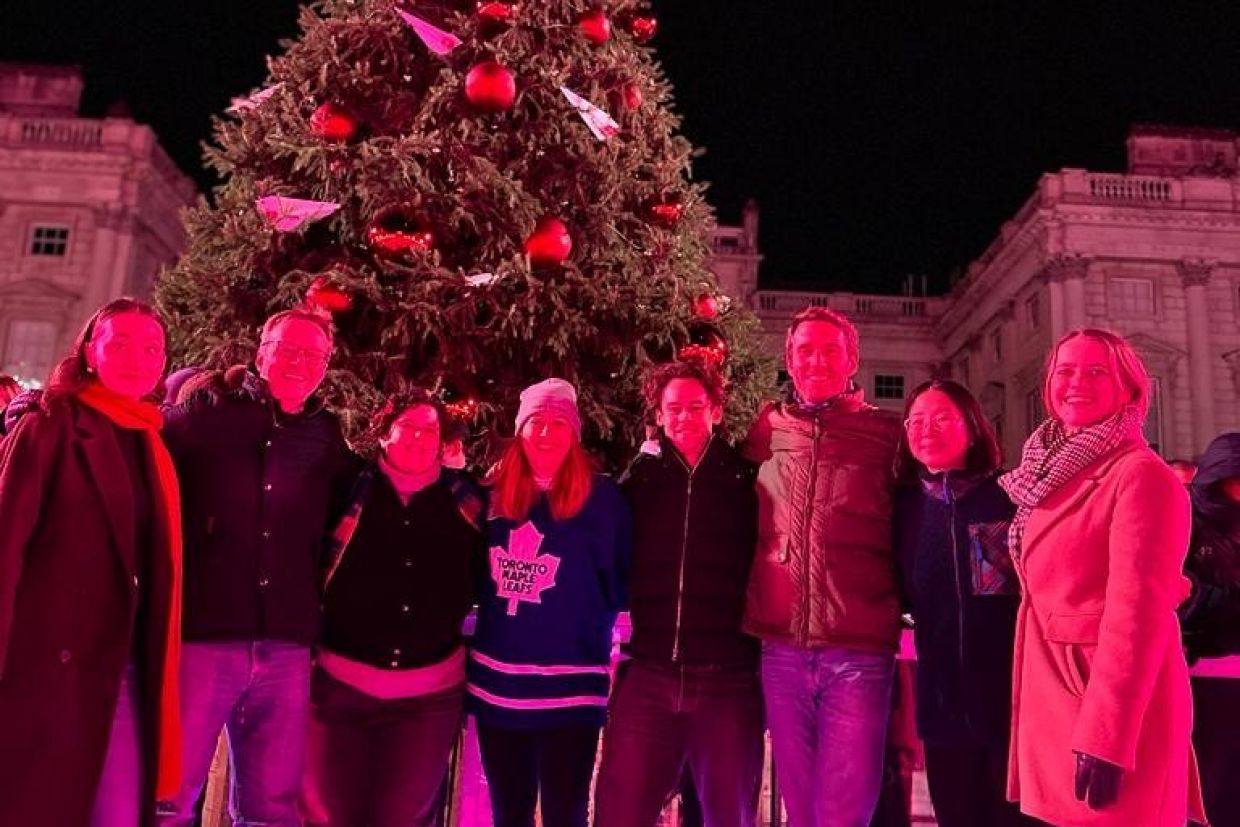 Alumni on a skating rink posing in front of a Christmas tree at night.