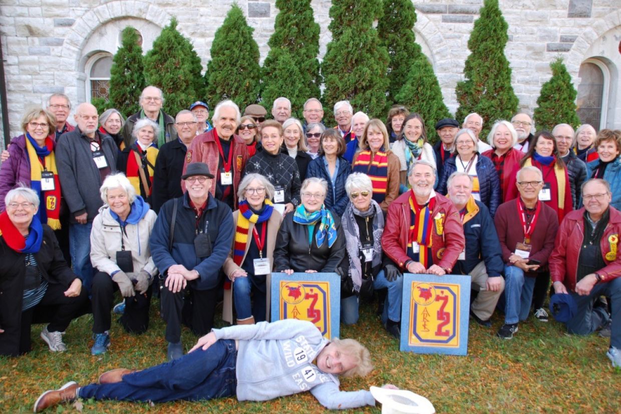 Arts'72 class photo in front of Grant Hall. The class is gathered behind the Arts'72 banner, with one member of the class laying in front of the banner on the grass.