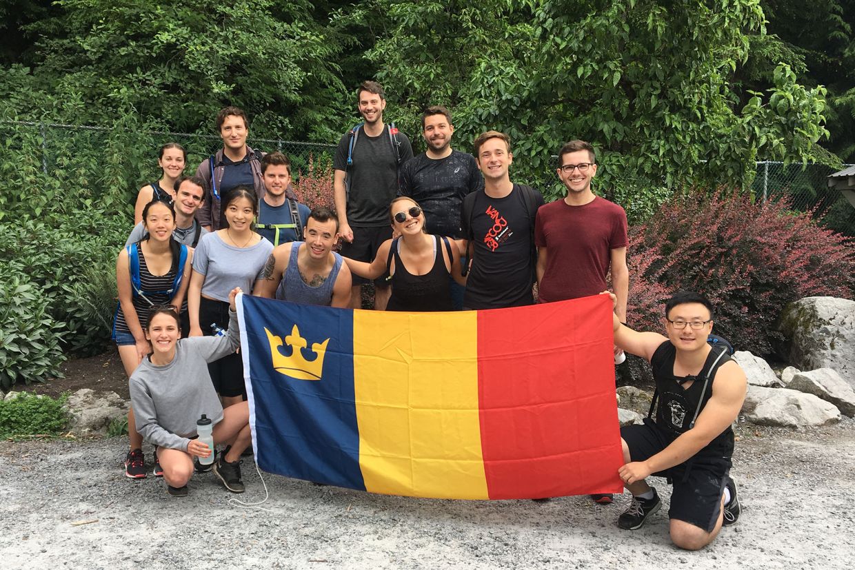 Queen's alumni pose outdoors with a Queen's alumni flag