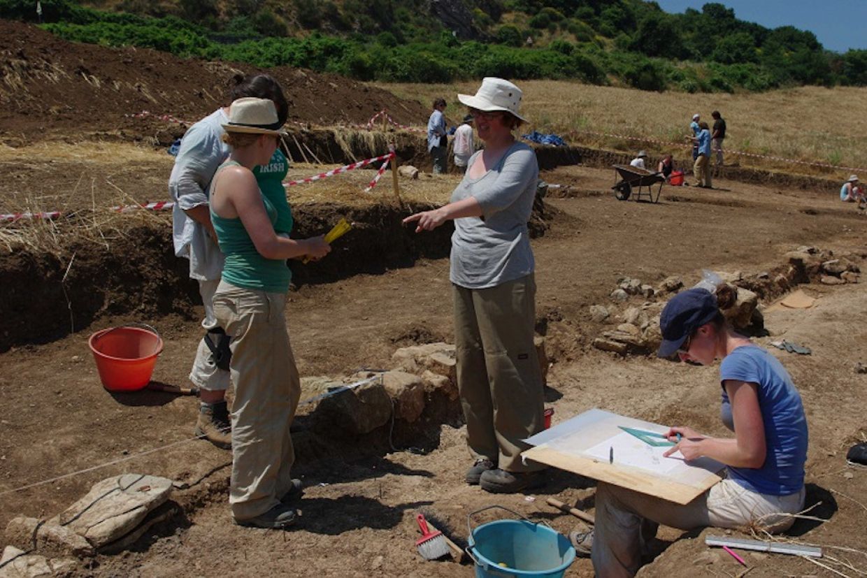 A group of students examine an object at an archaeological site.