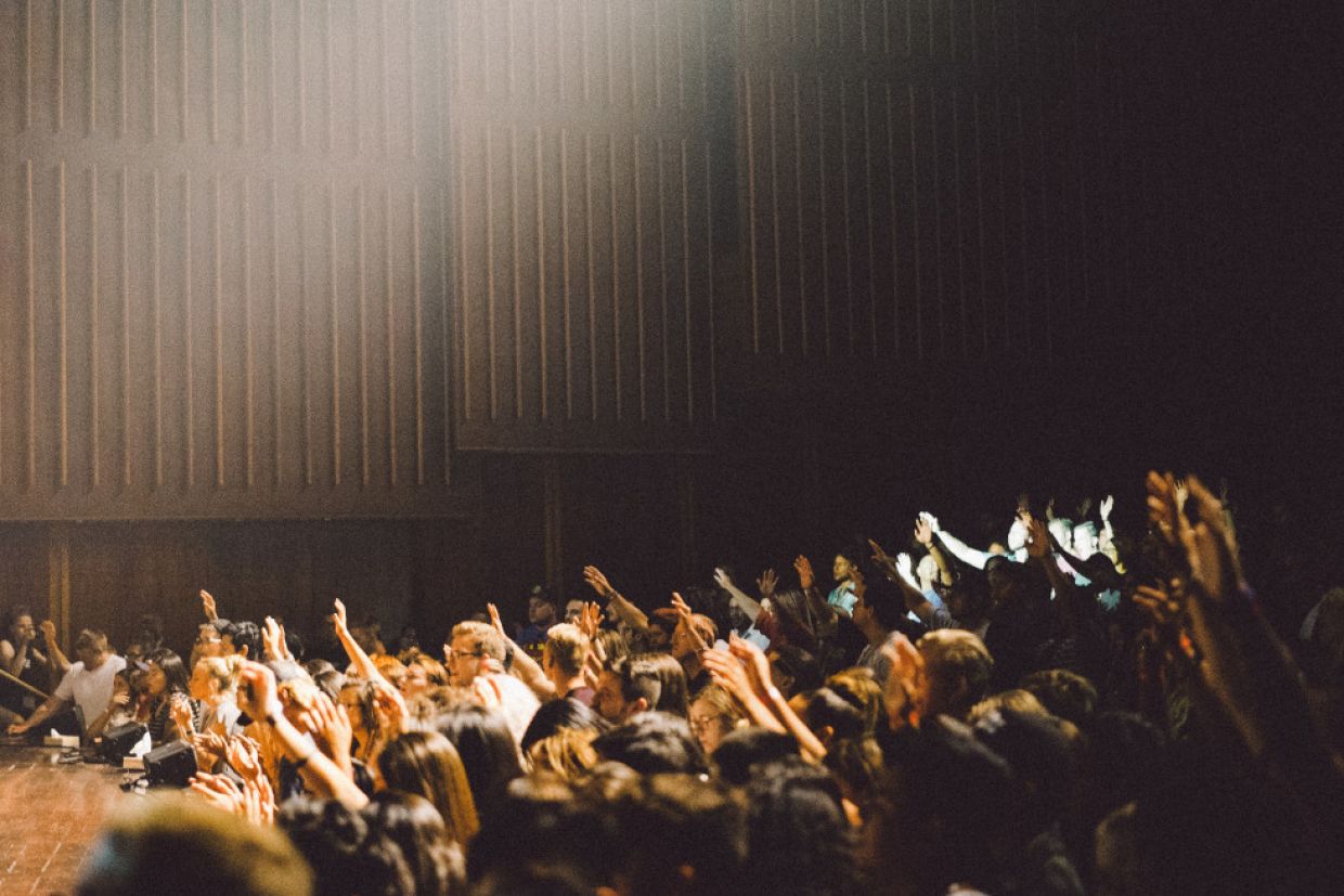 Students in a lecture hall raise their hands to answer a question.