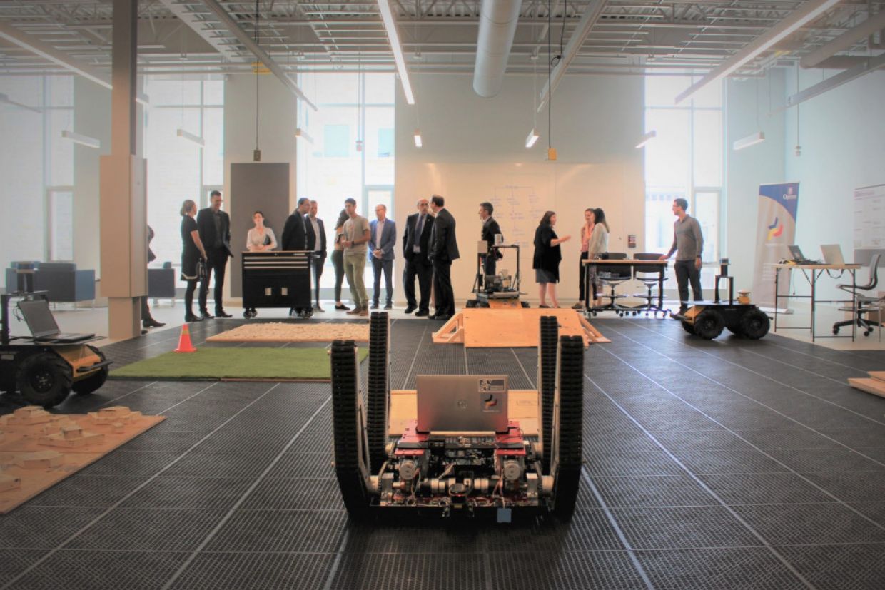 A short robot with wheels faces a room of people.