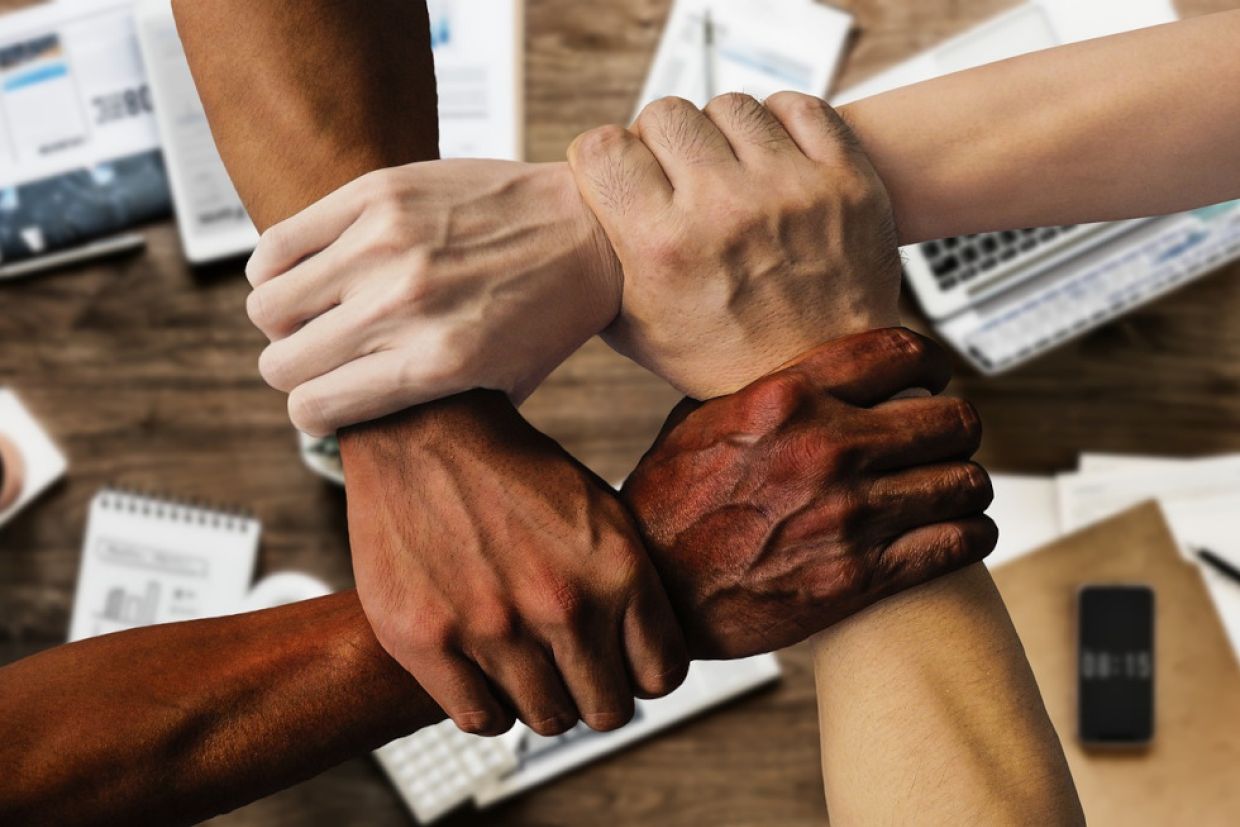 Diverse group of hands holding each other by the wrist forming a square.