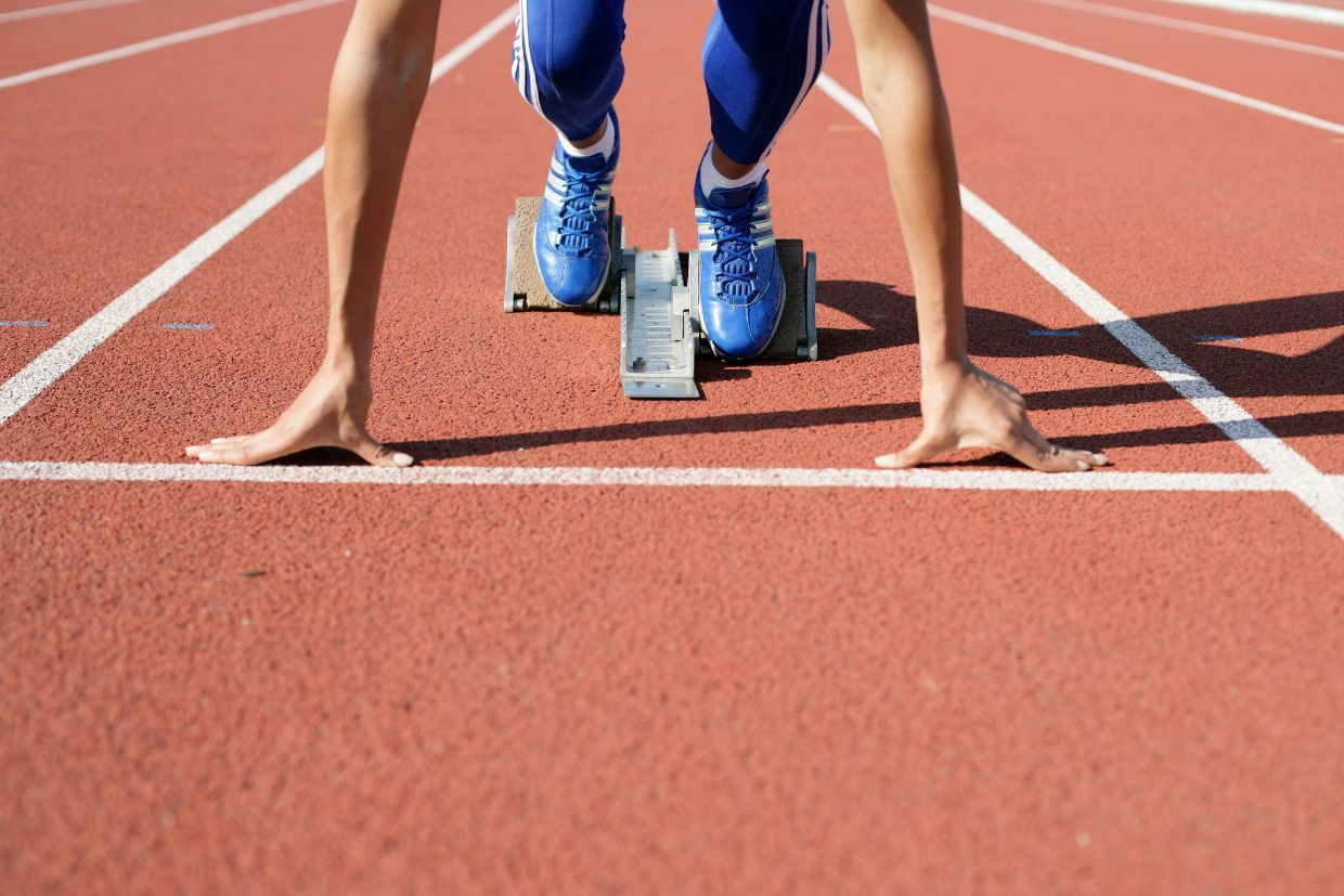 An athlete stands at the starting line on a running track, preparing to take off.