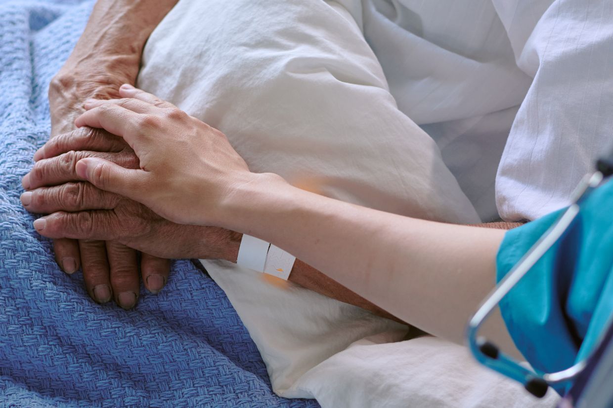 A medical care professional gently holds the hand of an elderly person, providing comfort and support in a caring environment.