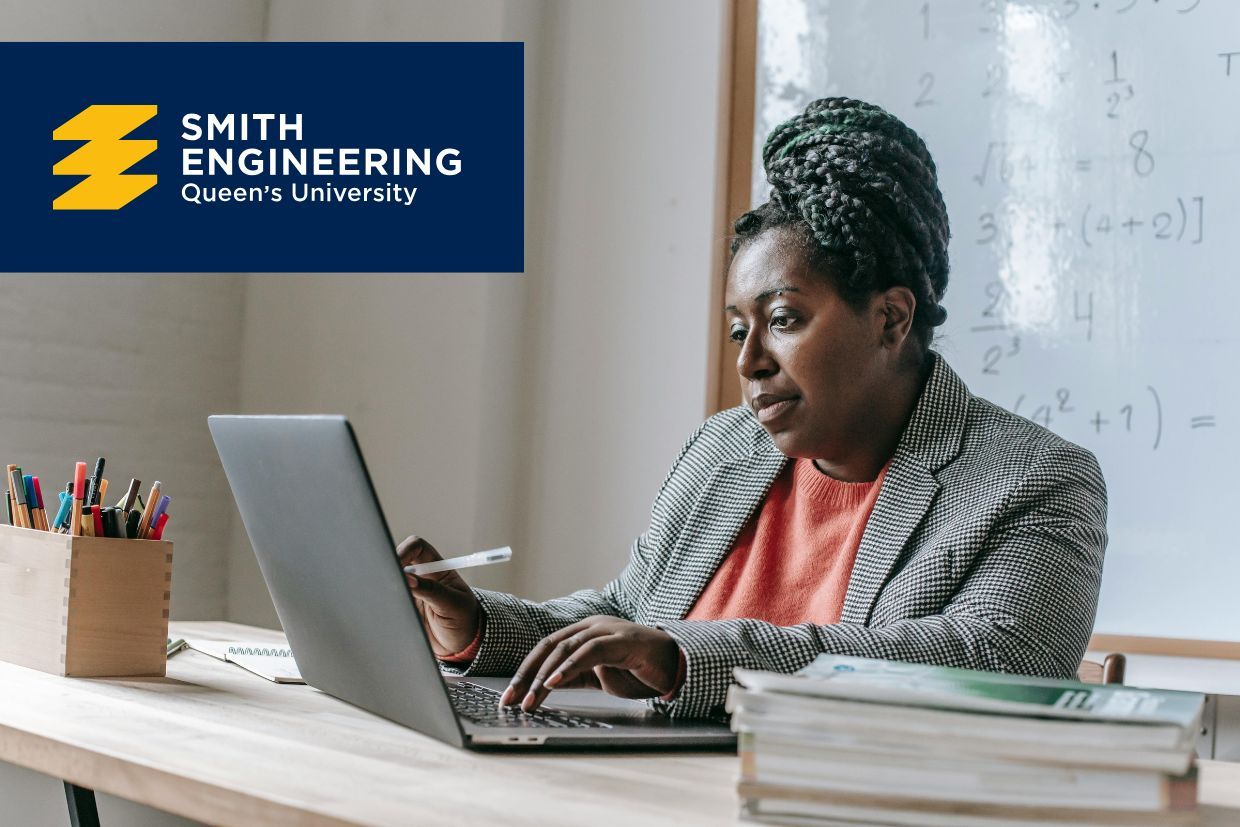 A person wearing a bright orange outfit and a grey jacket is watching a computer screen, accompanied by the Smith Engineering logo over a blue banner, with a school classroom in the background.