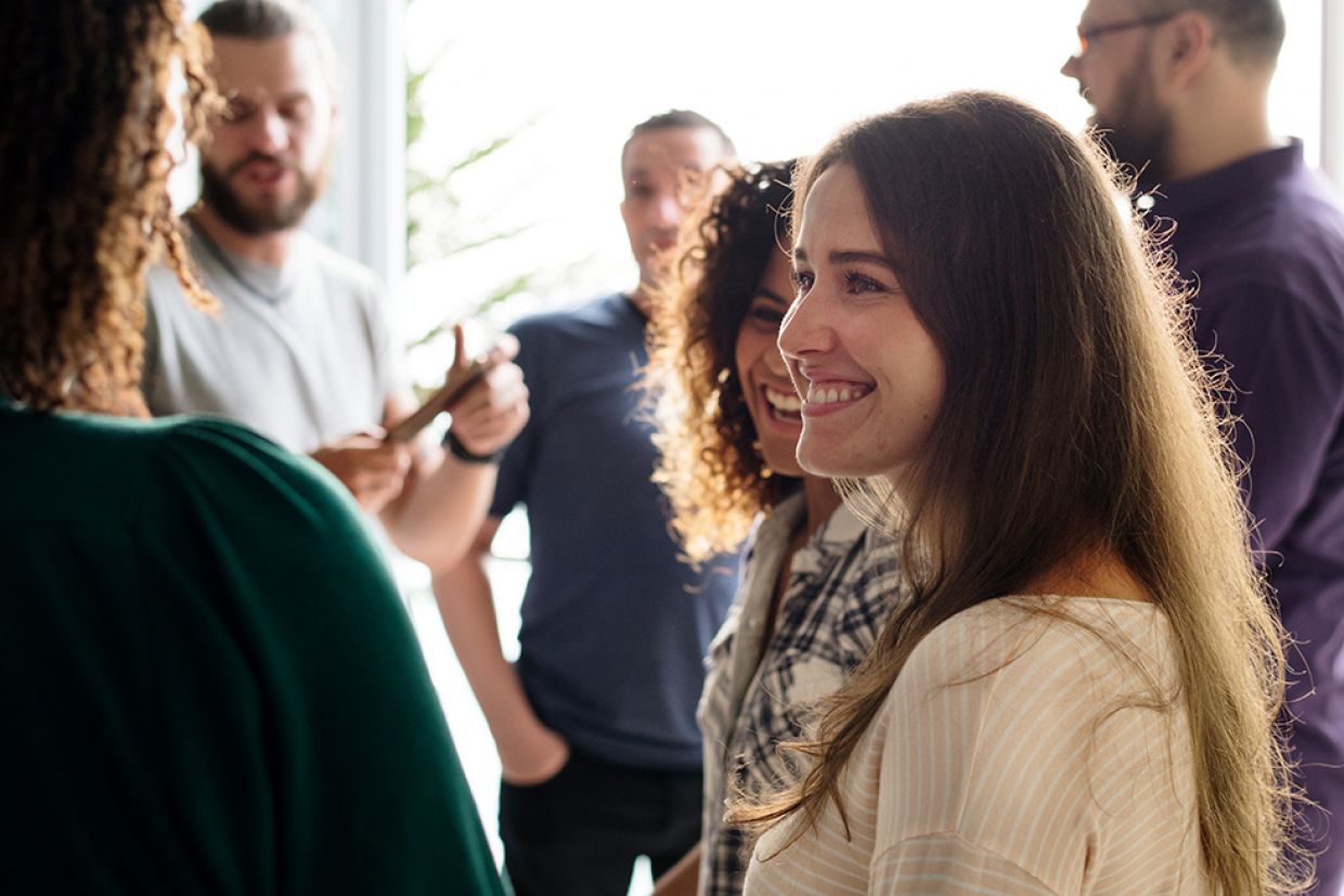 A person in conversation smiles. Others mingle in the background casually.