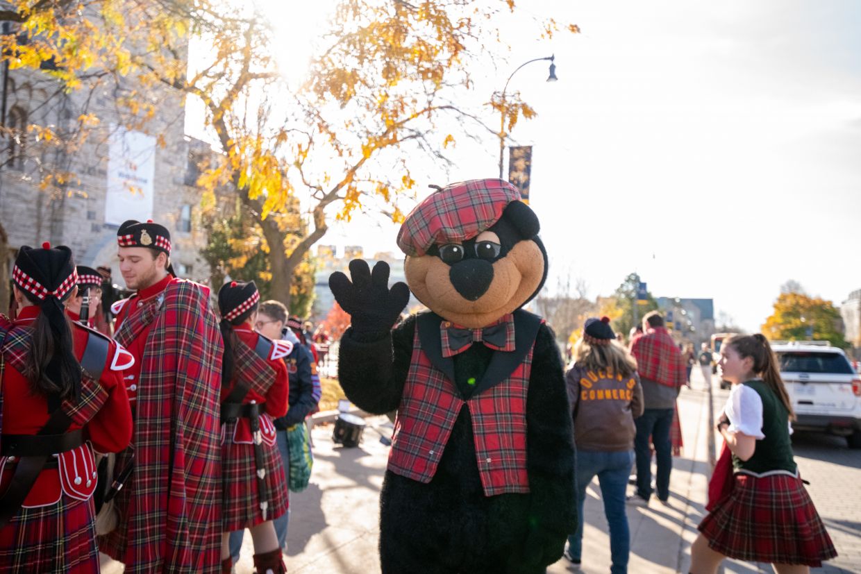 Photo of Boo Hoo the bear standing on the sidewalk waving at the camera.