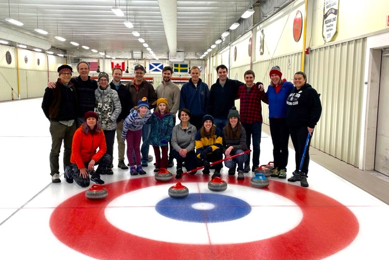 A group of alumni, family, and friends posed in front of the button on a curling rink
