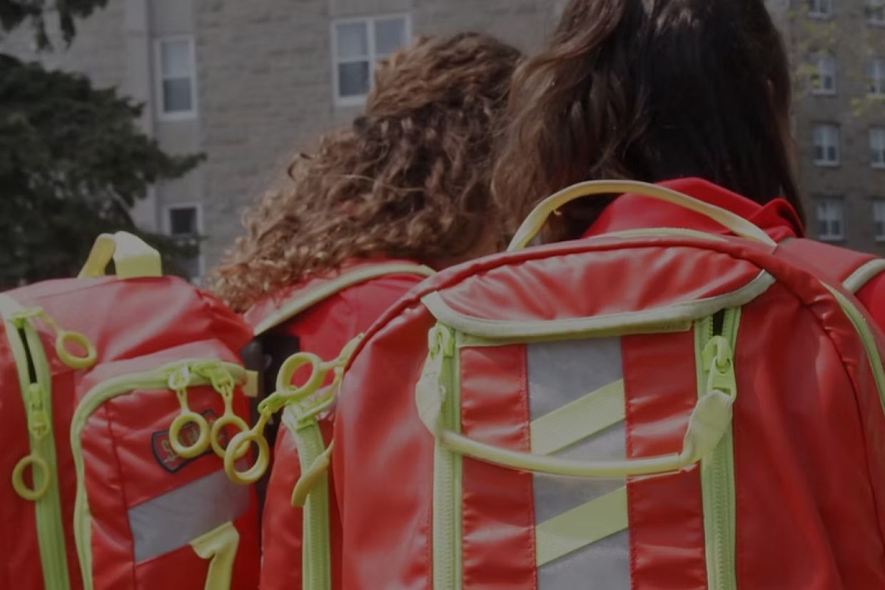 Two QFA volunteers with their bright orange backpacks on, backs to camera, facing Vic Hall