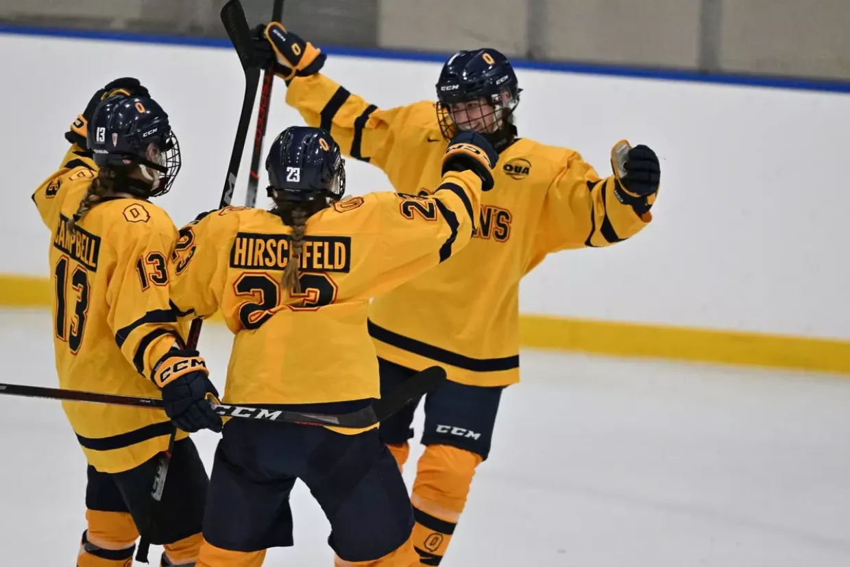 Three Queen's University Women's Hockey players celebrating together post-goal with arms in the air