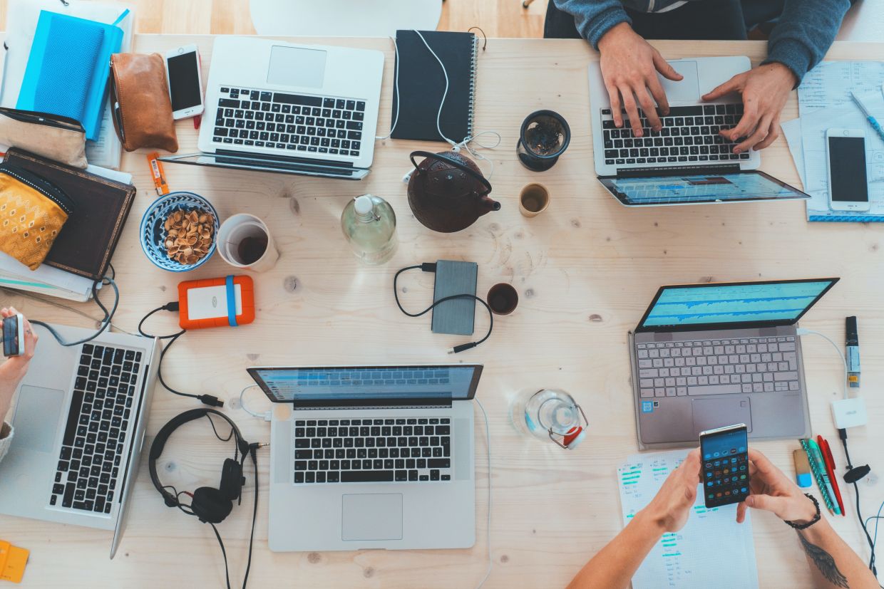 Aerial view of a desk featuring smart devices, snacks, and people working. 