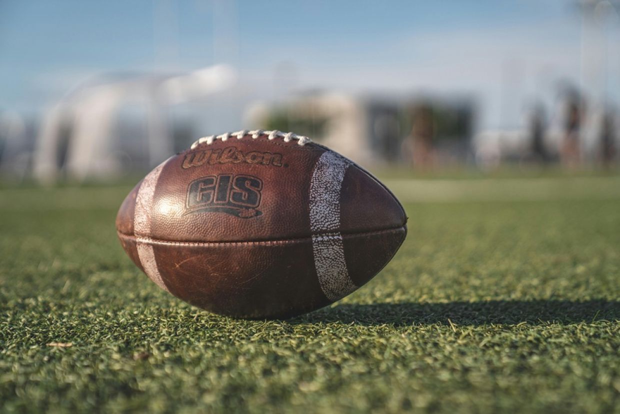 Close-up photo of a brown Wilson pigskin football on green turf with blurred background