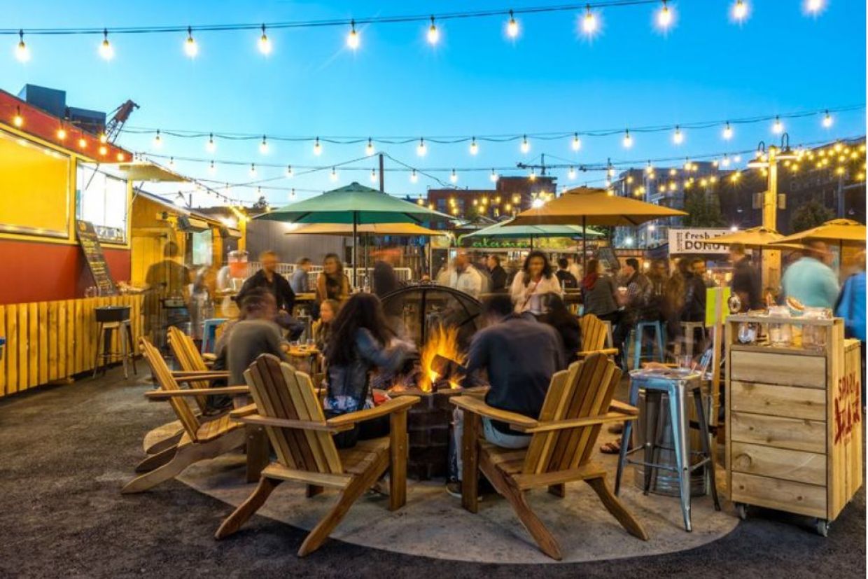 People sitting in chairs around an outdoor firepit on a patio at sunset.