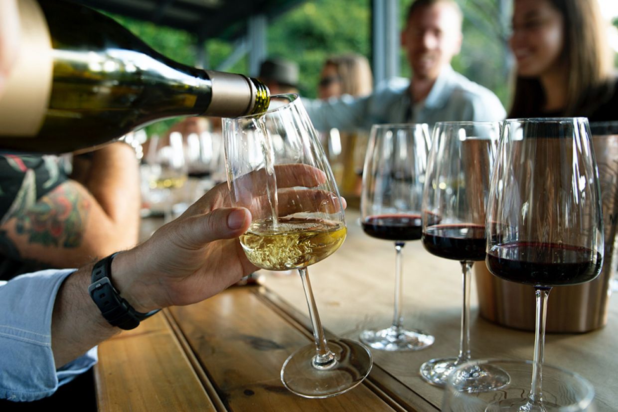 People sit at a table with glasses of wine as wine is poured from a bottle into a glass