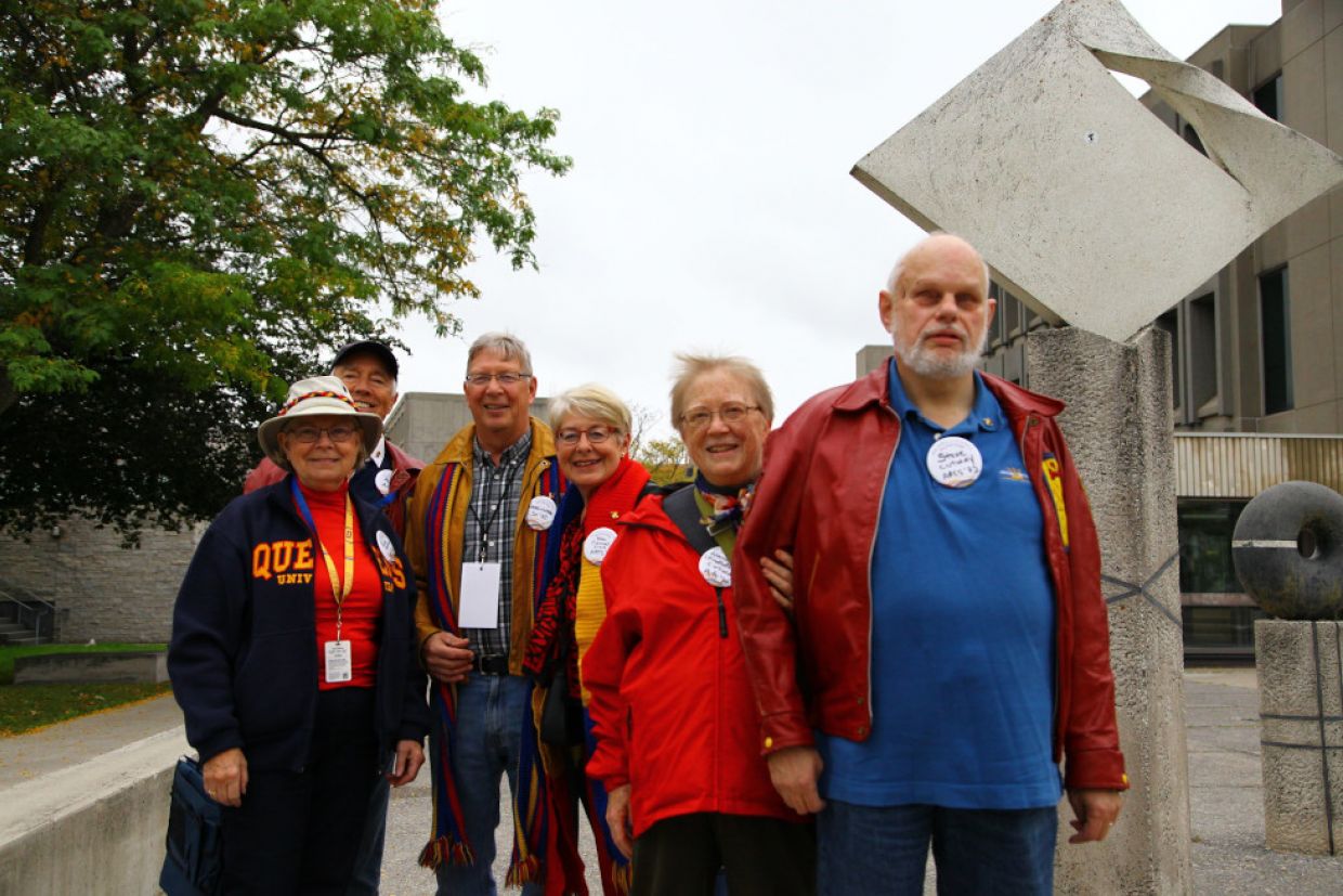Alumni in tricolour, wearing pins that say class year 1972 walk in front of Jeffrey Hall.