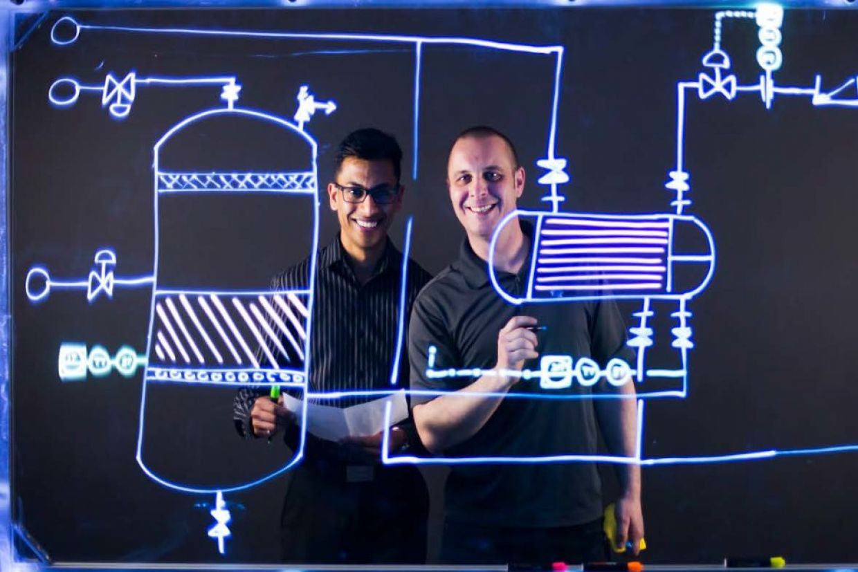 Two teachers writing work problems on a clear whiteboard