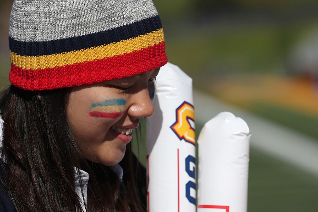 A young person where's a tricolour toque and has the alumni flag painted on her cheek. 