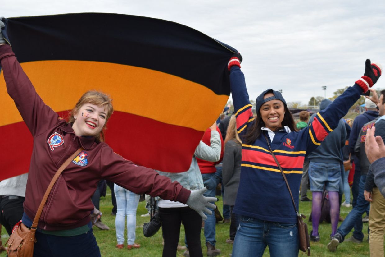 Students in tricolour hold a Queen's flag between them in a celebratory manner. 