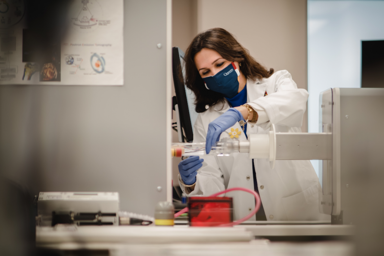 A woman in a lab coat, gloves, and mask works in the lab of the BioSciences Complex.