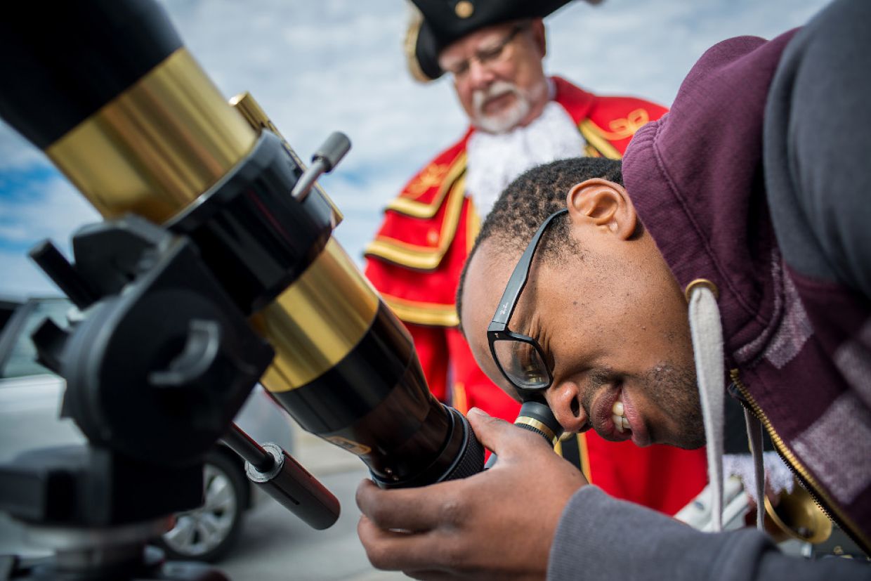 A man with a concentrated expression looks through a telescope. 