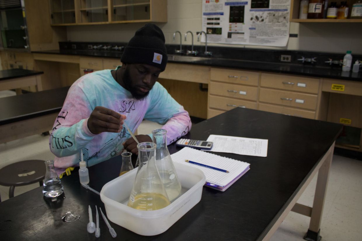 A student studies a beaker. A calculator and notebook are visible on the desk. 